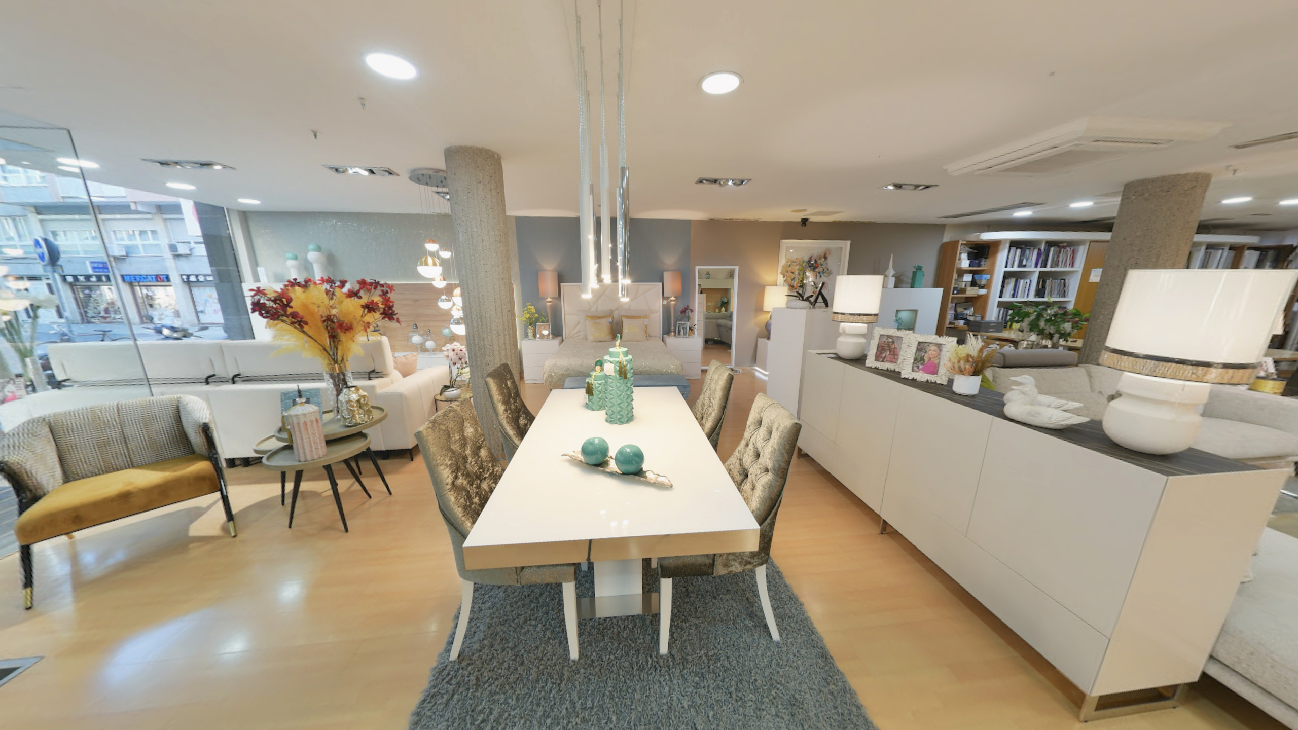 Tienda de Muebles en Barcelona, mobiliario a medida y diseño - Temas Mobiliario Vista de una amplia exposición de muebles que incluye una mesa de comedor blanca, un aparador moderno a la derecha y un sofá al fondo, con iluminación de diseño