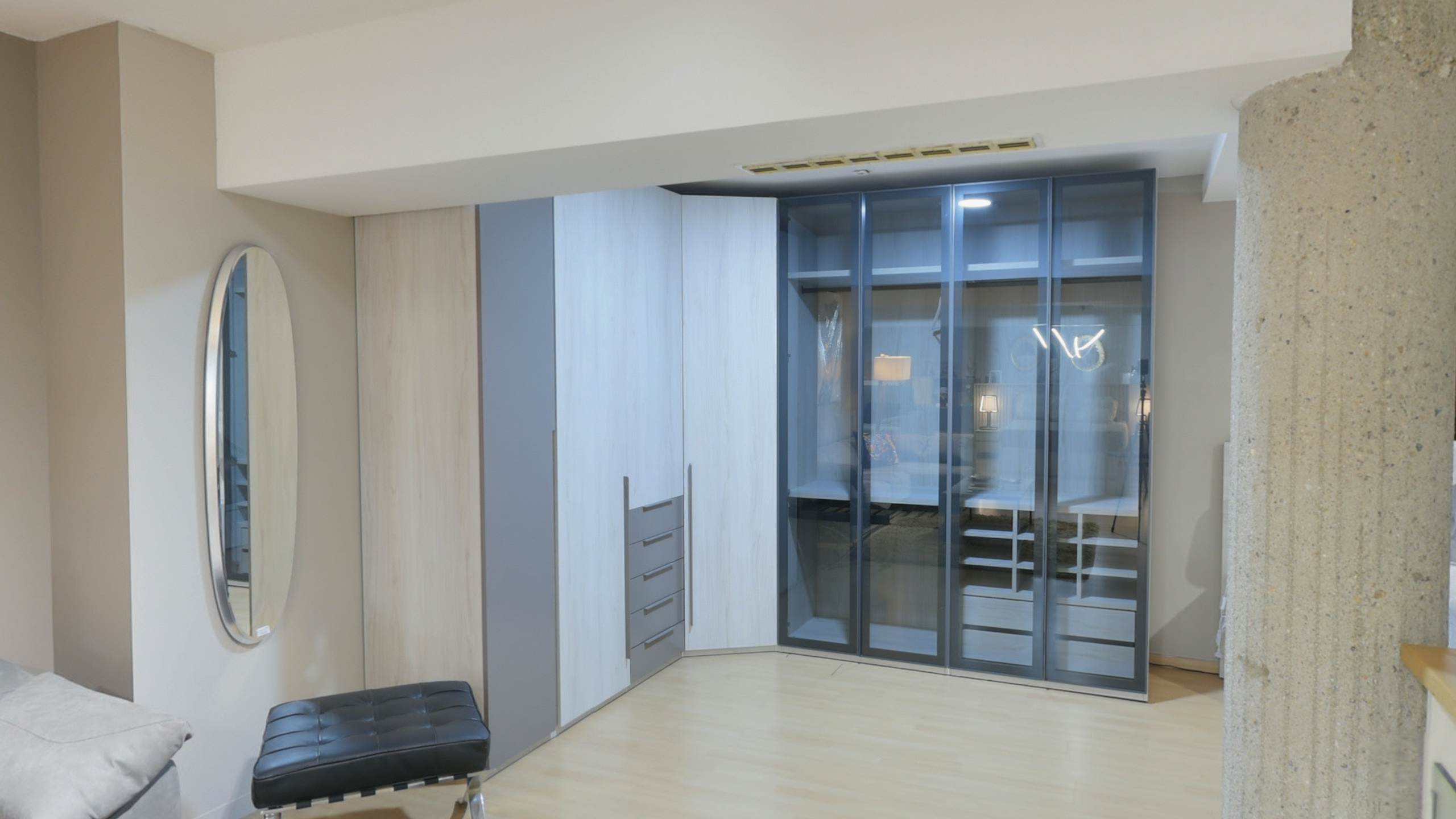 Tienda de Muebles en Barcelona, mobiliario a medida y diseño - Temas Mobiliario Armario esquinero a medida con una sección de puertas de cristal oscuro transparente que muestra estantes interiores, junto a módulos de madera clara y cajonera gris