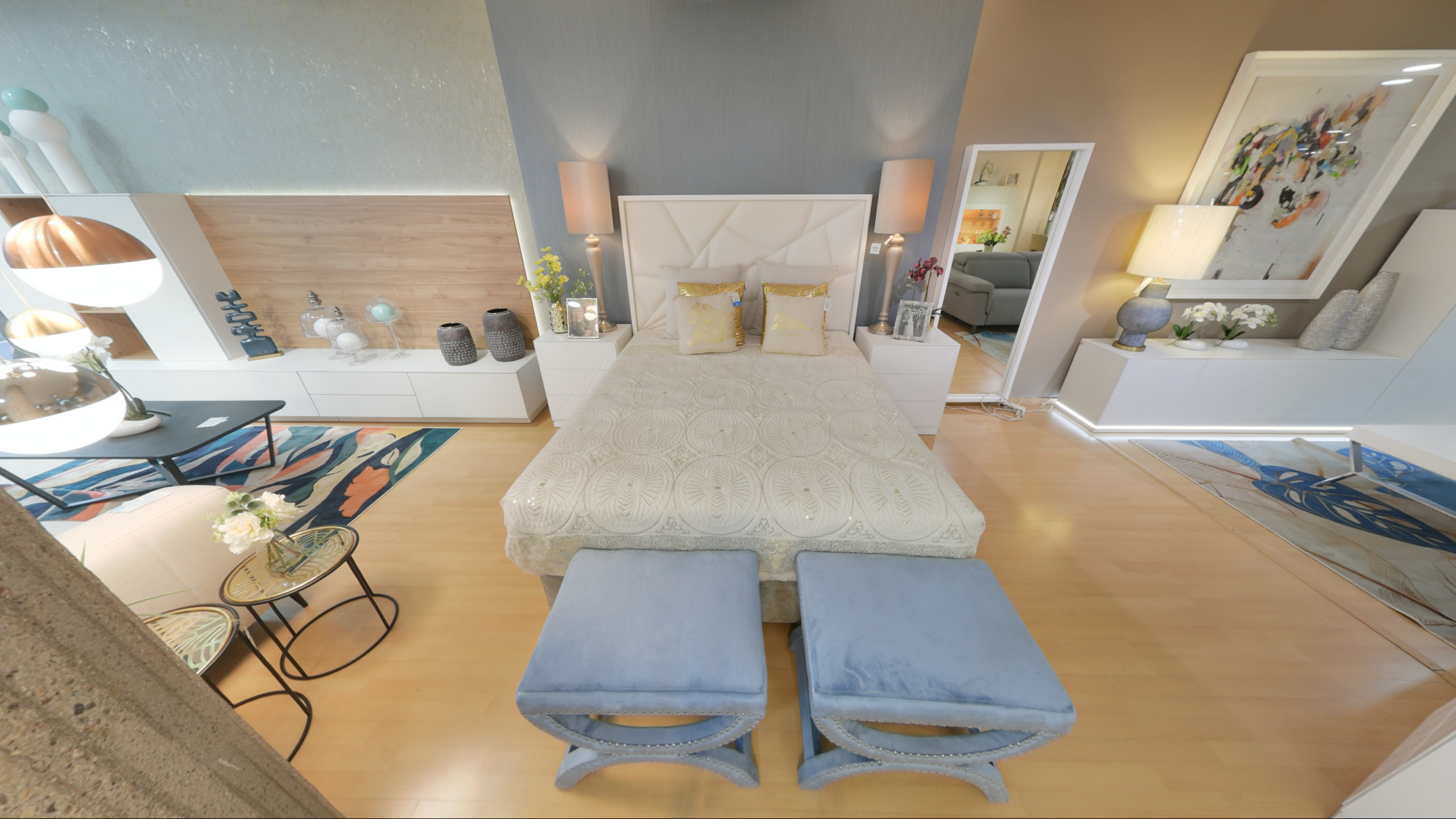 Tienda de Muebles en Barcelona, mobiliario a medida y diseño - Temas Mobiliario Cama de matrimonio con cabecero tapizado blanco de diseño geométrico, flanqueada por dos lámparas de pie elegantes y banquetas de terciopelo azul a los pies