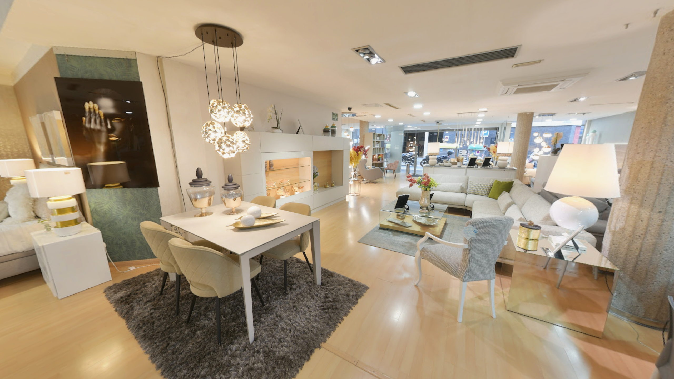 Tienda de Muebles en Barcelona, mobiliario a medida y diseño - Temas Mobiliario Vista de una amplia exposición de muebles que incluye una mesa de comedor blanca, un aparador moderno a la derecha y un sofá al fondo, con iluminación de diseño.