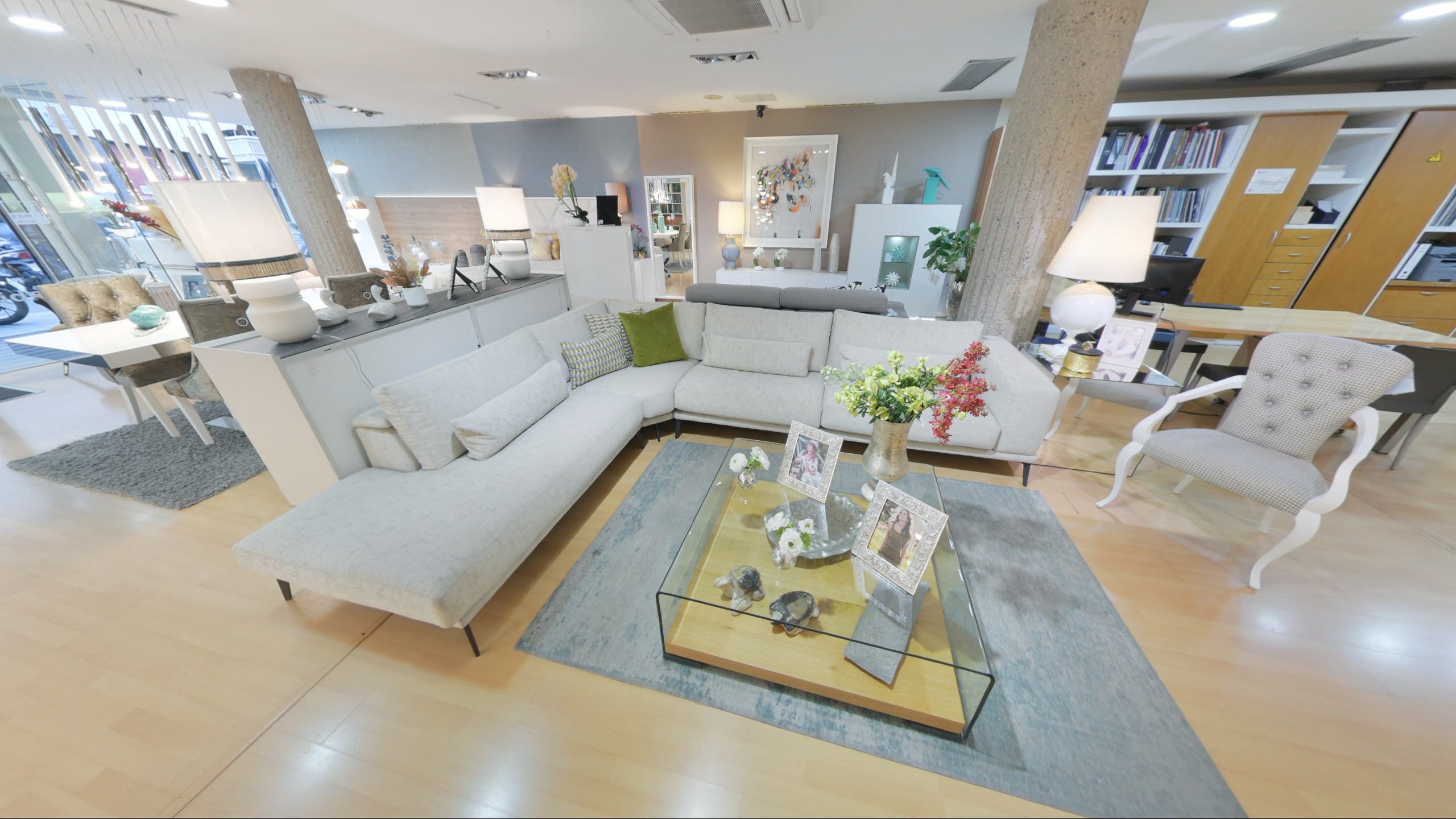 Tienda de Muebles en Barcelona, mobiliario a medida y diseño - Temas Mobiliario ofá rinconera modular en color gris claro con cojines decorativos y mesa de centro de cristal en exposición de interiorismo.