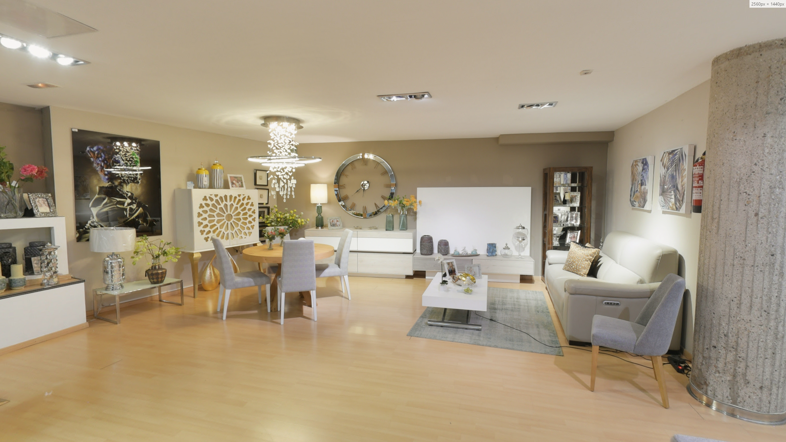 Tienda de Muebles en Barcelona, mobiliario a medida y diseño - Temas Mobiliario Conjunto de salón con mueble de TV blanco, mesa de comedor redonda y aparador con detalles geométricos bajo una lámpara de araña moderna.